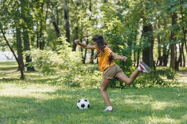 Vista lateral del niño pateando pelota de fútbol en el parque - foto de stock
