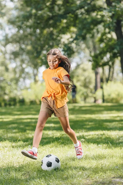 Чарівна усміхнена дитина грає з футбольним м'ячем у парку — стокове фото