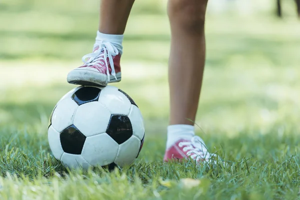 Plan recadré de l'enfant debout avec ballon de football sur l'herbe — Photo de stock