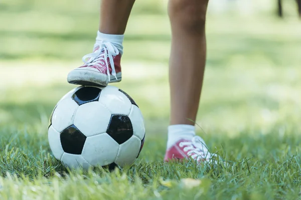 Recortado tiro de niño de pie con pelota de fútbol en la hierba - foto de stock