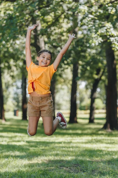 Очаровательный счастливый ребенок прыгает и улыбается на камеру в парке — стоковое фото