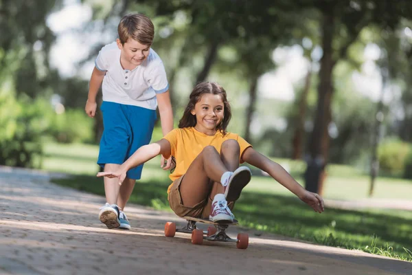 Adorable happy children having fun with longboard in park — Stock Photo