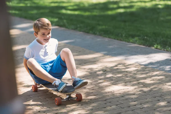 Vista de ángulo alto de lindo niño sonriente sentado en el monopatín en el parque - foto de stock