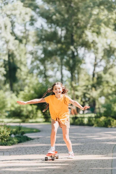 Schönes glückliches Kind fährt Skateboard und lächelt in die Kamera im Park — Stockfoto