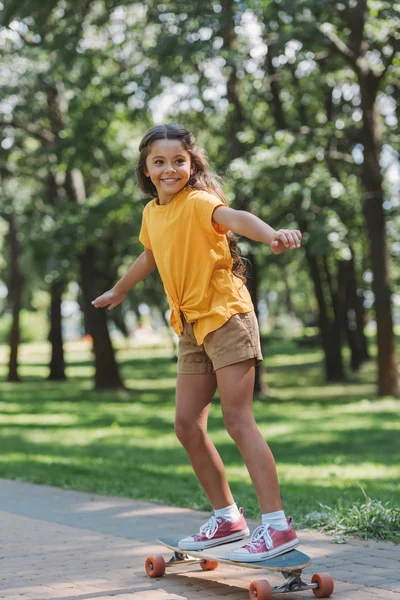 Красивый улыбающийся ребенок верхом на длинной доске в парке — стоковое фото