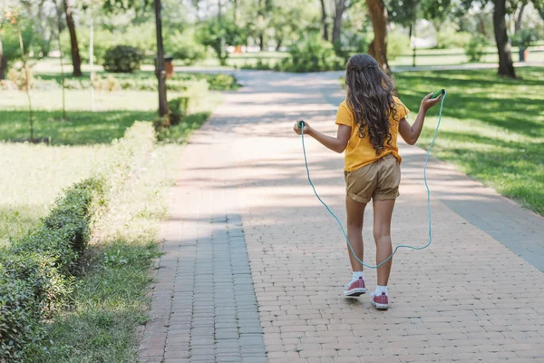 Vue arrière de mignon enfant marchant avec corde sautante dans le parc — Photo de stock