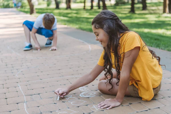 Adorable smiling children drawing with chalk in park — Stock Photo