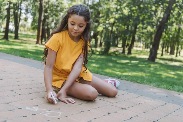 Красива дитина сидить і малює крейдою в парку — стокове фото