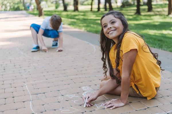 Adorable happy child drawing with chalk and looking away in park — Stock Photo