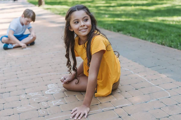 Niedliche glückliche Kinder zeichnen mit Kreide im Park — Stockfoto