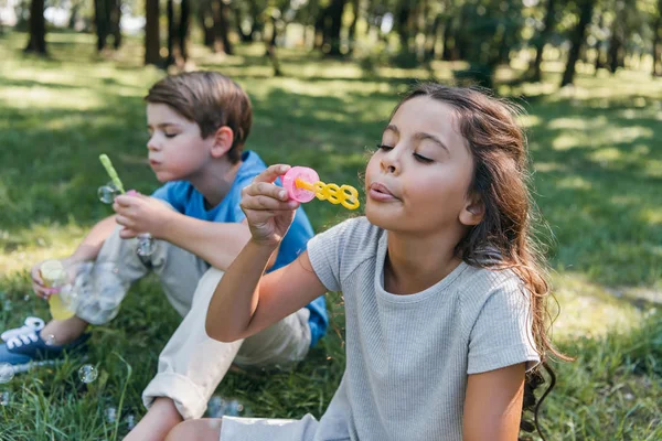 Adorable kids sitting and blowing soap bubbles in park — Stock Photo