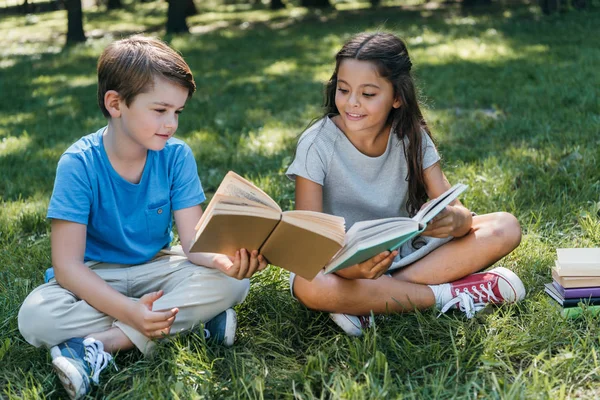 Niños pequeños y lindos sentados en la hierba y leyendo libros - foto de stock
