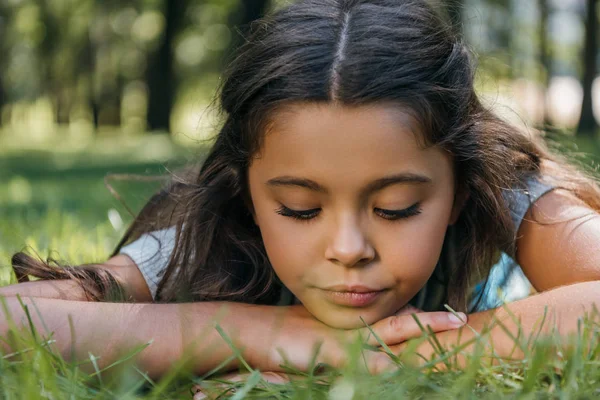 Nahaufnahme eines entzückenden Kindes, das im Gras liegt und im Park nach unten schaut — Stockfoto