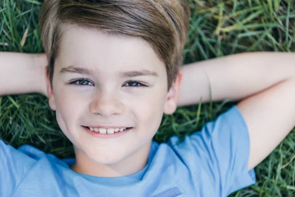 Top view of happy child lying on grass and smiling at camera — Stock Photo