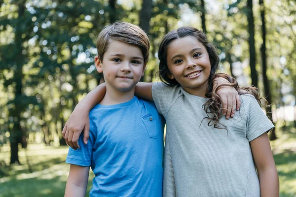 Schöne glückliche Kinder, die sich im Park umarmen und in die Kamera lächeln — Stockfoto