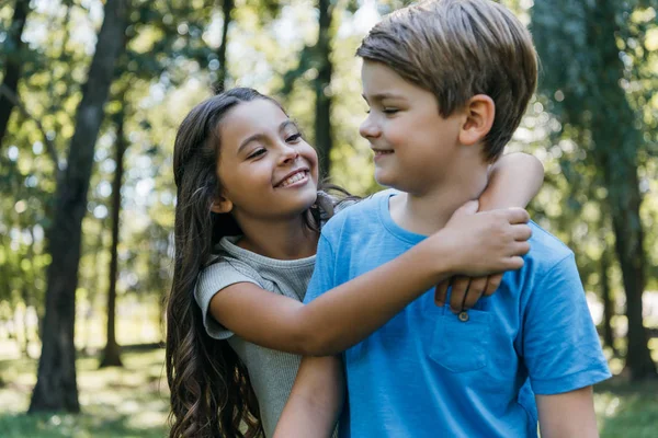 Милые счастливые дети обнимаются и улыбаются в парке — стоковое фото