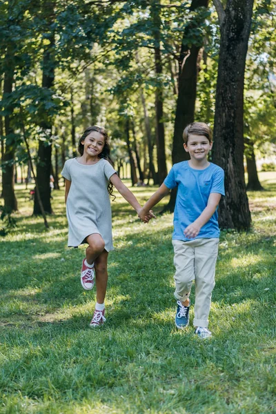 Adorable happy kids holding hands and running together in park — Stock Photo