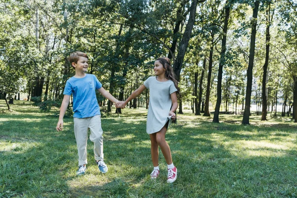 Entzückende glückliche Kinder, die sich im Park an den Händen halten und einander anlächeln — Stockfoto