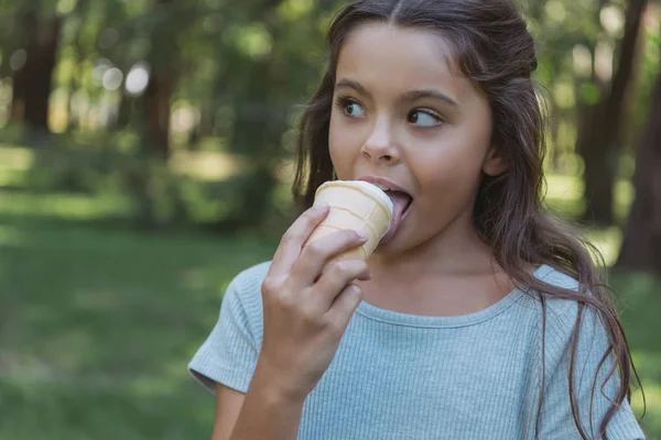 Adorable niño comiendo helado y mirando hacia otro lado en parque - foto de stock