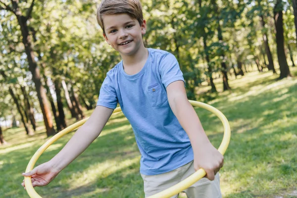 Happy boy playing with hula hoop and smiling at camera in park — Stock Photo