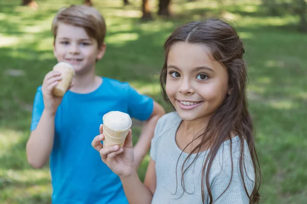 Adorables enfants heureux manger de la crème glacée et regarder la caméra dans le parc — Photo de stock