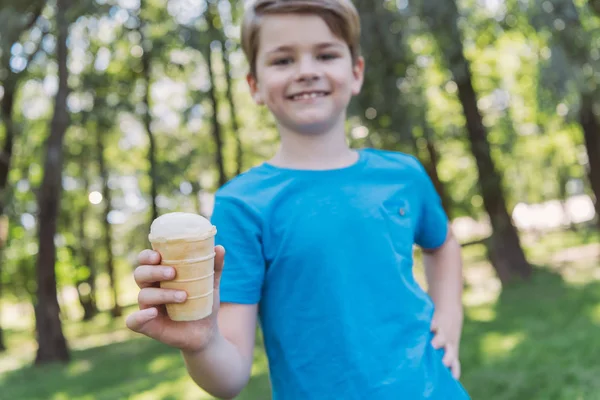 Vista ravvicinata di bambino felice che tiene il gelato e sorride alla macchina fotografica nel parco — Foto stock