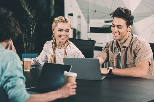 Empresários sorridentes que trabalham à mesa com laptops e xícaras de café no escritório moderno — Fotografia de Stock