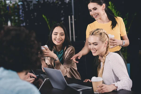 Sonriente mujer de negocios señalando en la pantalla del ordenador portátil a dos mujeres de negocios en la oficina moderna — Stock Photo