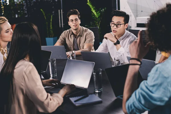 Multicultural group of business partners having discussion at table with laptops in modern office — Stock Photo