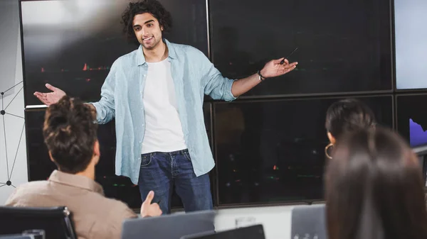 Joven hombre de negocios sonriente con brazos anchos mostrando la presentación a los socios de negocios en la oficina moderna — Stock Photo