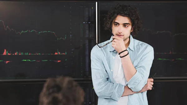 Joven hombre de negocios con gafas en la mano de pie delante del tablero con gráficos en la oficina moderna - foto de stock