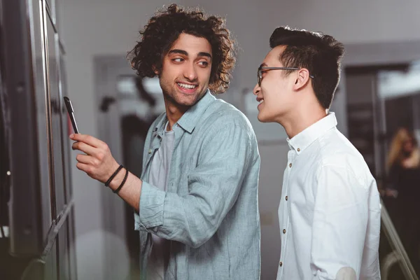 Joven empresario apuntando por pluma a bordo a asiático colega en moderno oficina - foto de stock