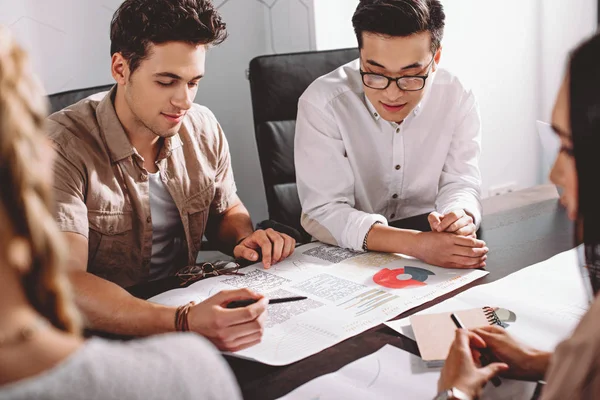 Two multiethnic businessmen having meeting at table with graphs in modern office — Stock Photo