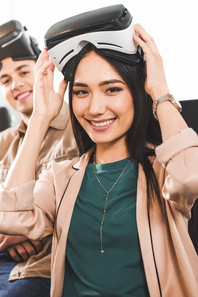 Socios comerciales multiétnicos con auriculares de realidad virtual en la mesa con ordenadores portátiles en la oficina moderna - foto de stock