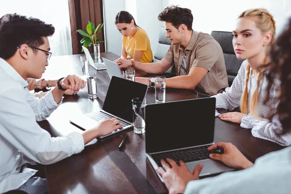 Multicultural business partners having meeting at table with laptops and glasses of water in modern office — Stock Photo