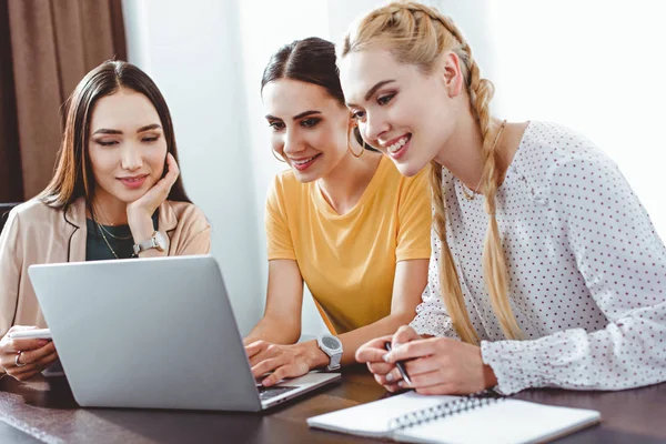 Trois femmes d'affaires multiculturelles utilisant un ordinateur portable à la table dans un bureau moderne — Photo de stock