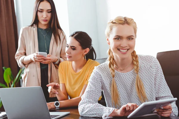 Усміхнена бізнес-леді з цифровим планшетом і її колегами позаду в сучасному офісі — стокове фото