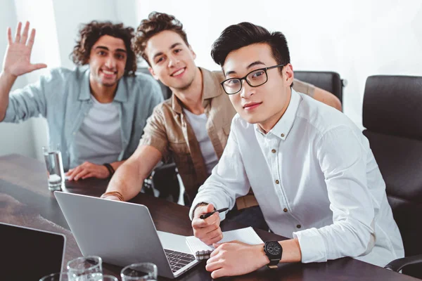 Trois hommes d'affaires multiculturels à table avec des ordinateurs portables dans un bureau moderne — Photo de stock