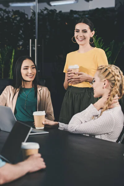 Partenaires d'affaires multiculturels avec des tasses en papier de café ayant réunion à table avec des ordinateurs portables dans le bureau moderne — Photo de stock