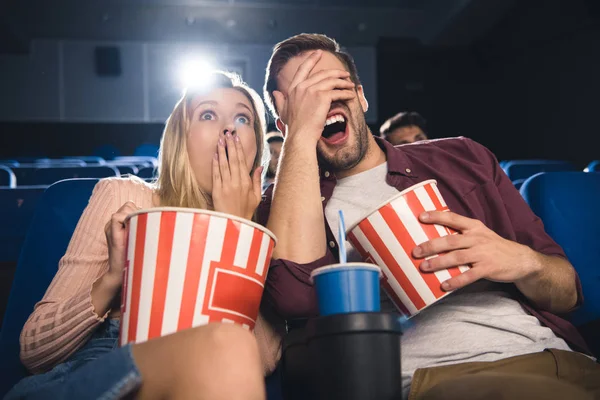 Scared couple with popcorn and soda drink watching film together in cinema — Stock Photo