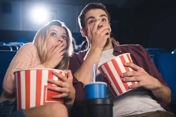 Scared couple with popcorn and soda drink watching film together in cinema — Stock Photo