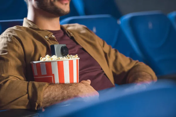 Vue partielle de l'homme avec une petite caméra vidéo dans le pop-corn tournage illégal film au cinéma — Photo de stock