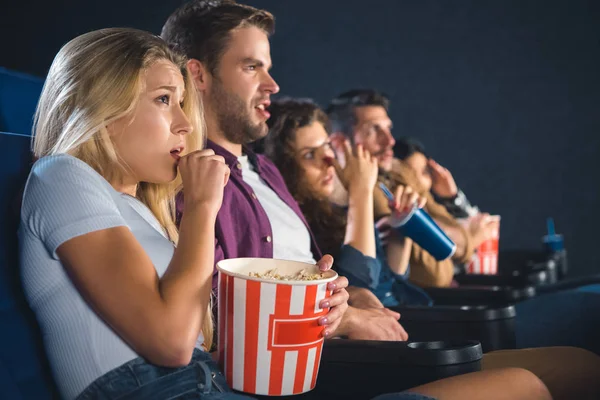 Amigos multiétnicos assustados com pipocas assistindo filme juntos no cinema — Fotografia de Stock