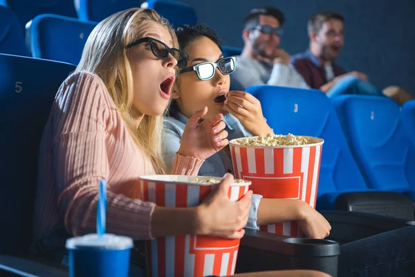 Shocked multiracial women in 3d glasses with popcorn watching film together in movie theater — Stock Photo