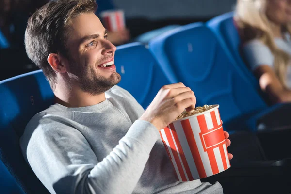 Side view of cheerful man with popcorn watching film in cinema — Stock Photo