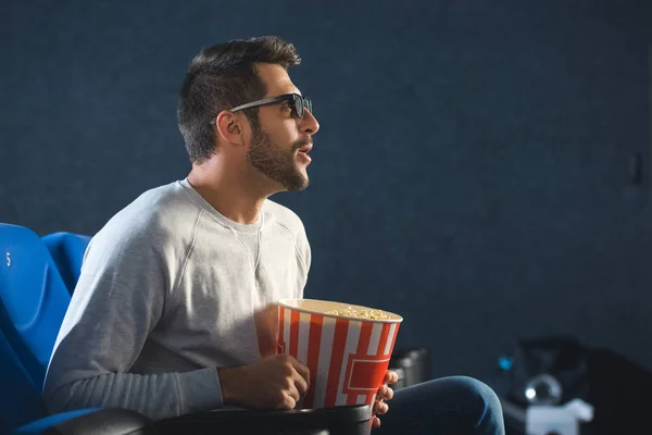 Seitenansicht eines emotionalen Mannes in 3D-Gläsern mit Popcorn, der sich allein im Kino Filme ansieht — Stockfoto