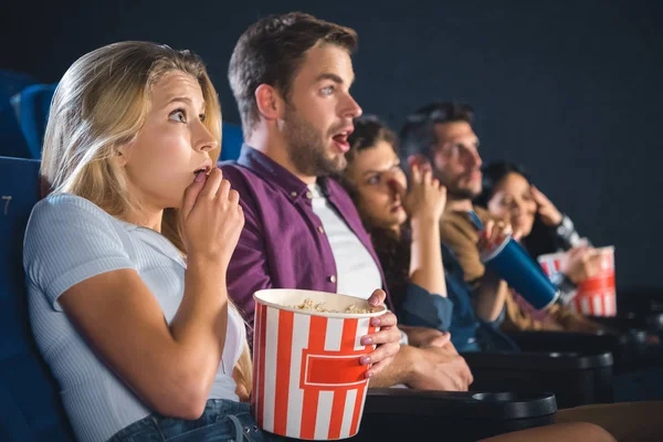 Scared multiethnic friends with popcorn watching film together in movie theater — Stock Photo