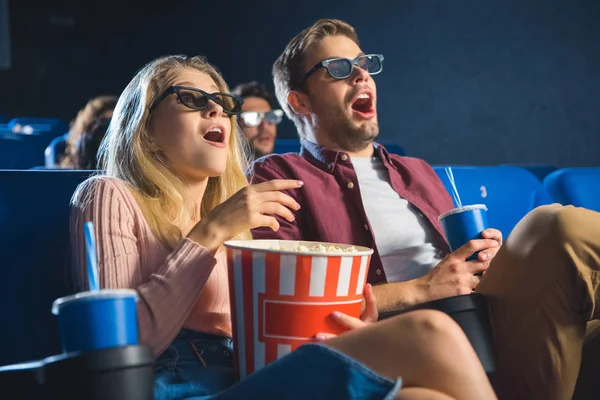 Couple choqué dans des lunettes 3D avec pop-corn regarder le film ensemble au cinéma — Photo de stock