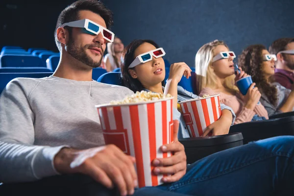 Amigos multiétnicos en gafas 3D con palomitas de maíz viendo películas juntos en el cine - foto de stock