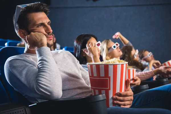 Bored multiethnic friends with popcorn watching film together in movie theater — Stock Photo
